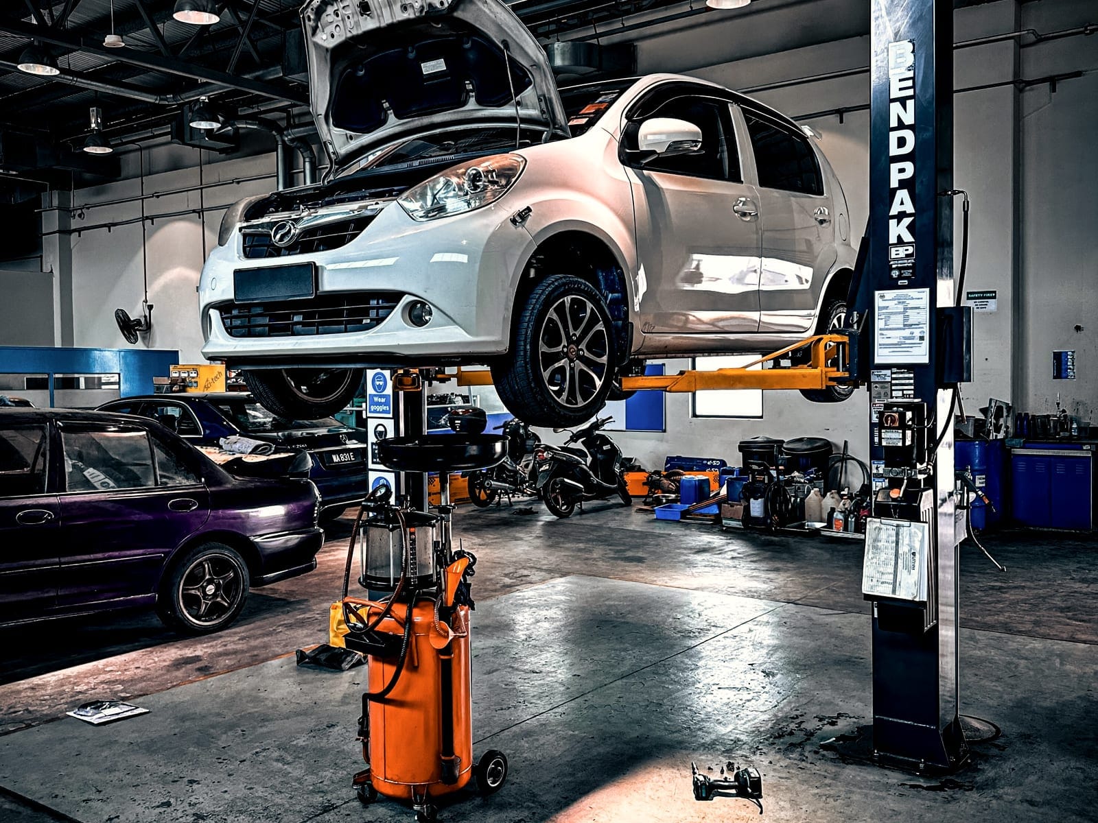 Auto uniesione na podnośniku dwukolumnowym, w tle stanowiska warsztatu